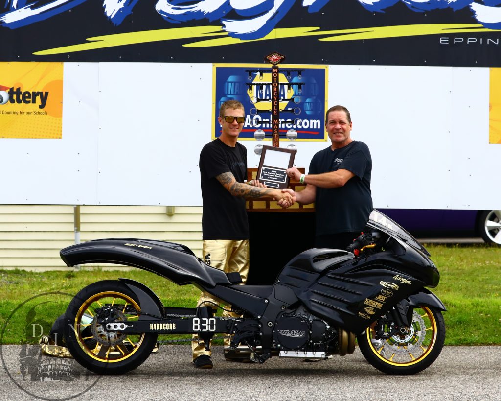 Joe & Chris Pratt photo: Joe Ferraro is greeted in the New England Dragway winner’s circle by Chris Pratt of Just Wood Flooring, Newfields NH, to receive his plaque for winning the 5th annual New England Dragway Motorcycle Masters race. Joe’s name will be engraved into the Motorcycle Masters trophy as he now ranks among the best of the best at New England Dragway, in Epping, NH. Tom McCarthy photo.